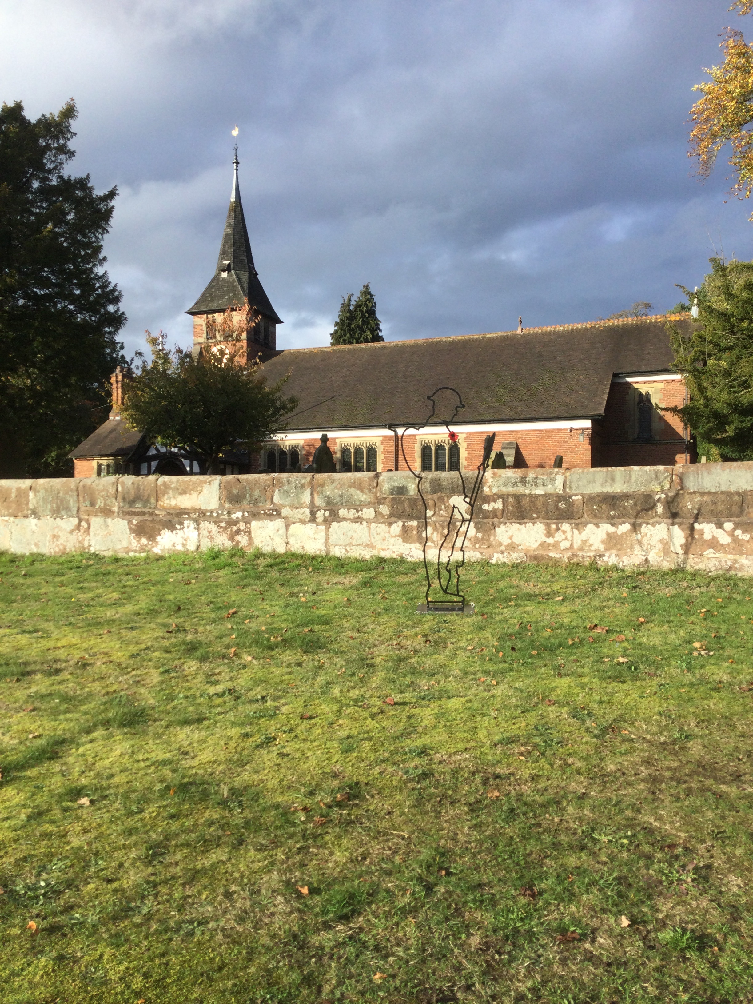 Outline of a soldier standing in front of the churchyard wall with the church in the background.
