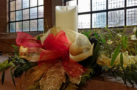 Candle, ribbon and foliage arrangement on church window sill.